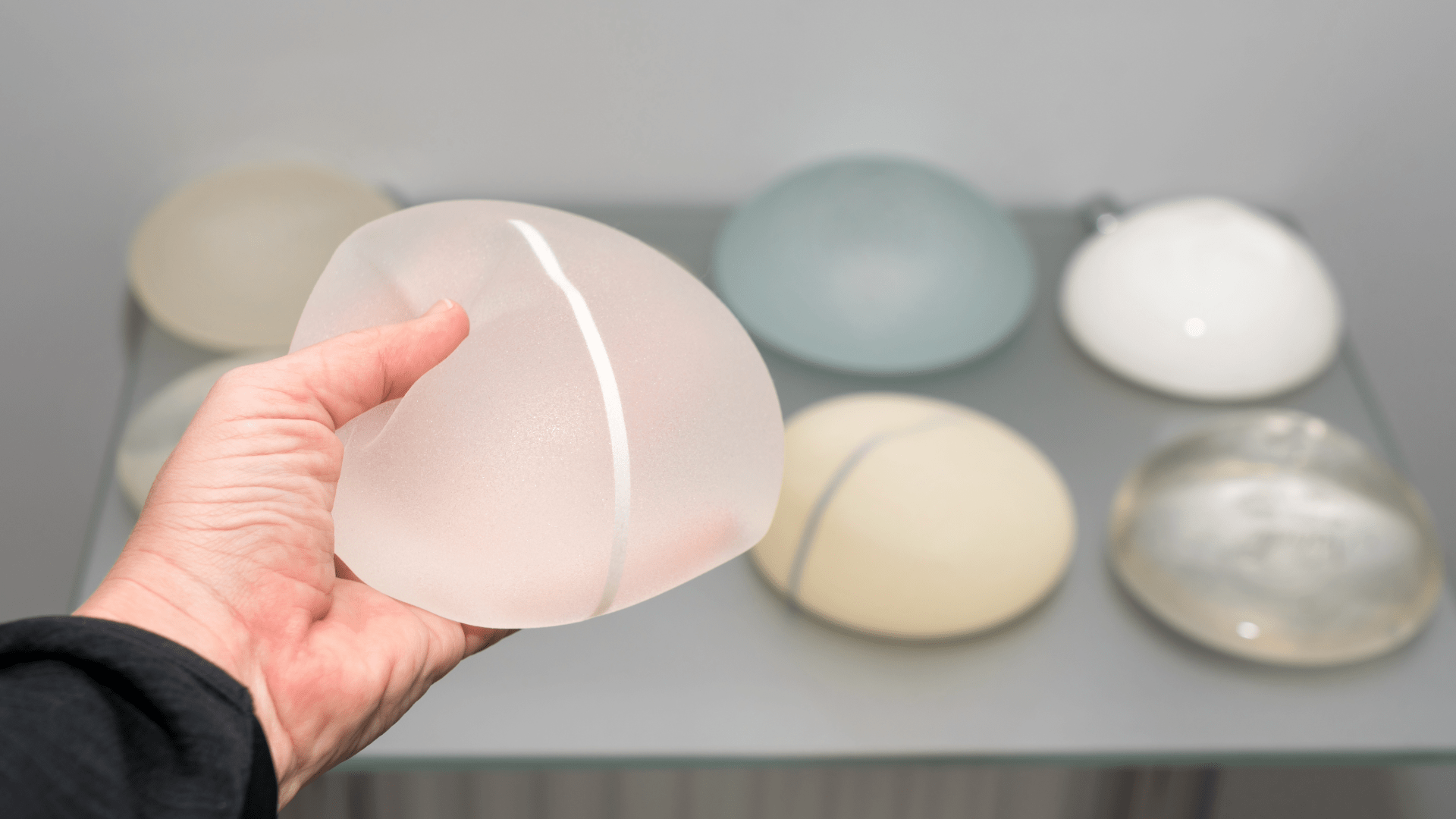 Hand holding a pale pink frosted glass bowl with a white stripe, with other decorative bowls blurred in the background on a shelf.
