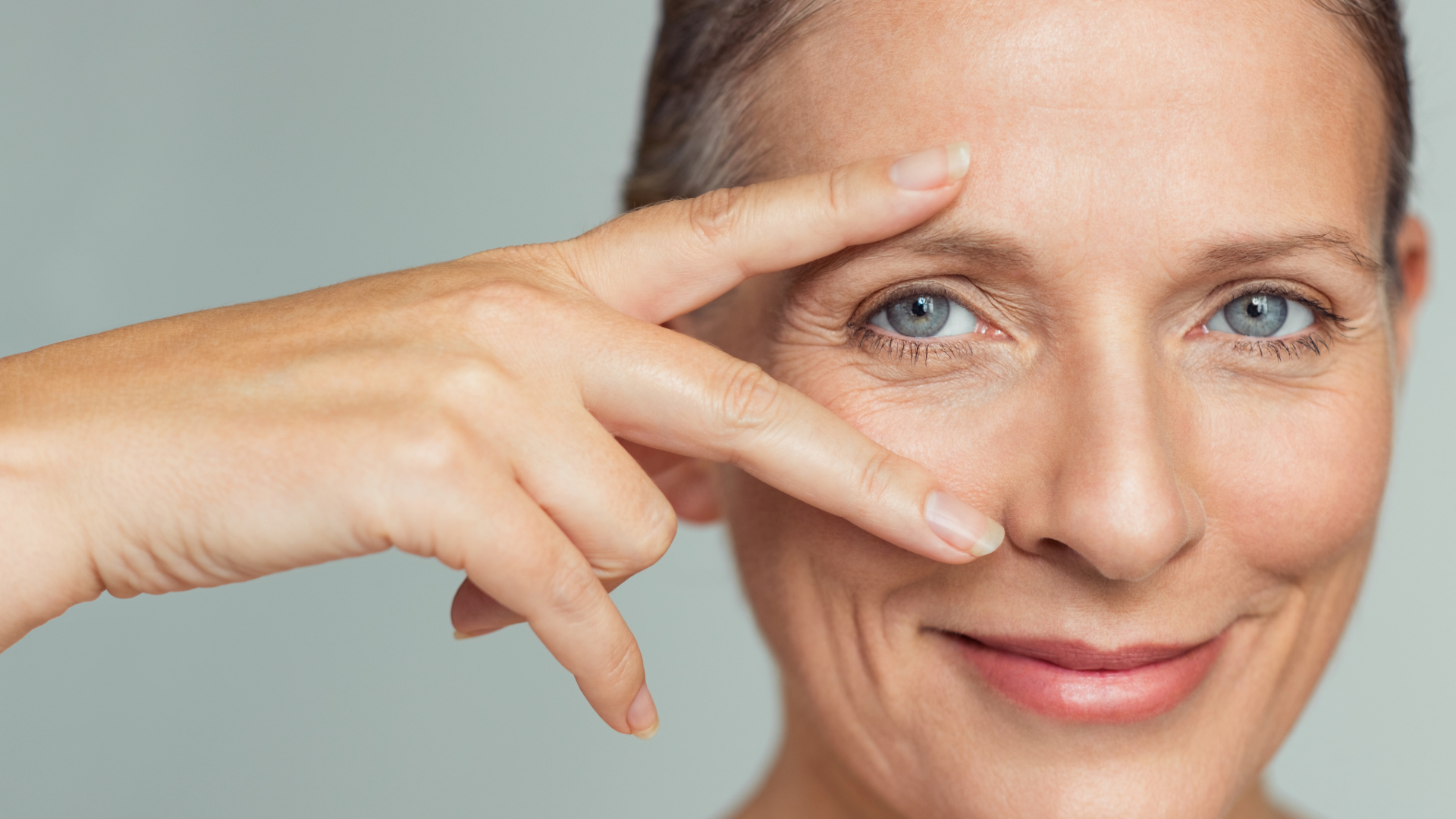 Close-up of a smiling woman with blue eyes, fingers forming a V near her eye.