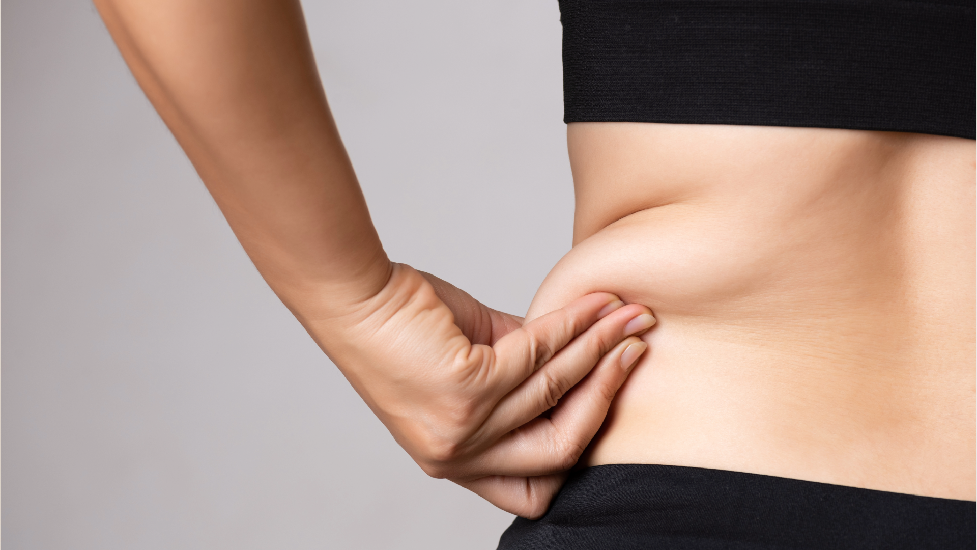 Close-up of a hand pinching abdominal fat at the waist area.