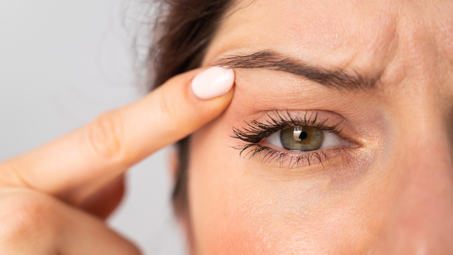 Close-up of a person pulling down the lower eyelid to reveal a green eye with visible lashes and skin texture