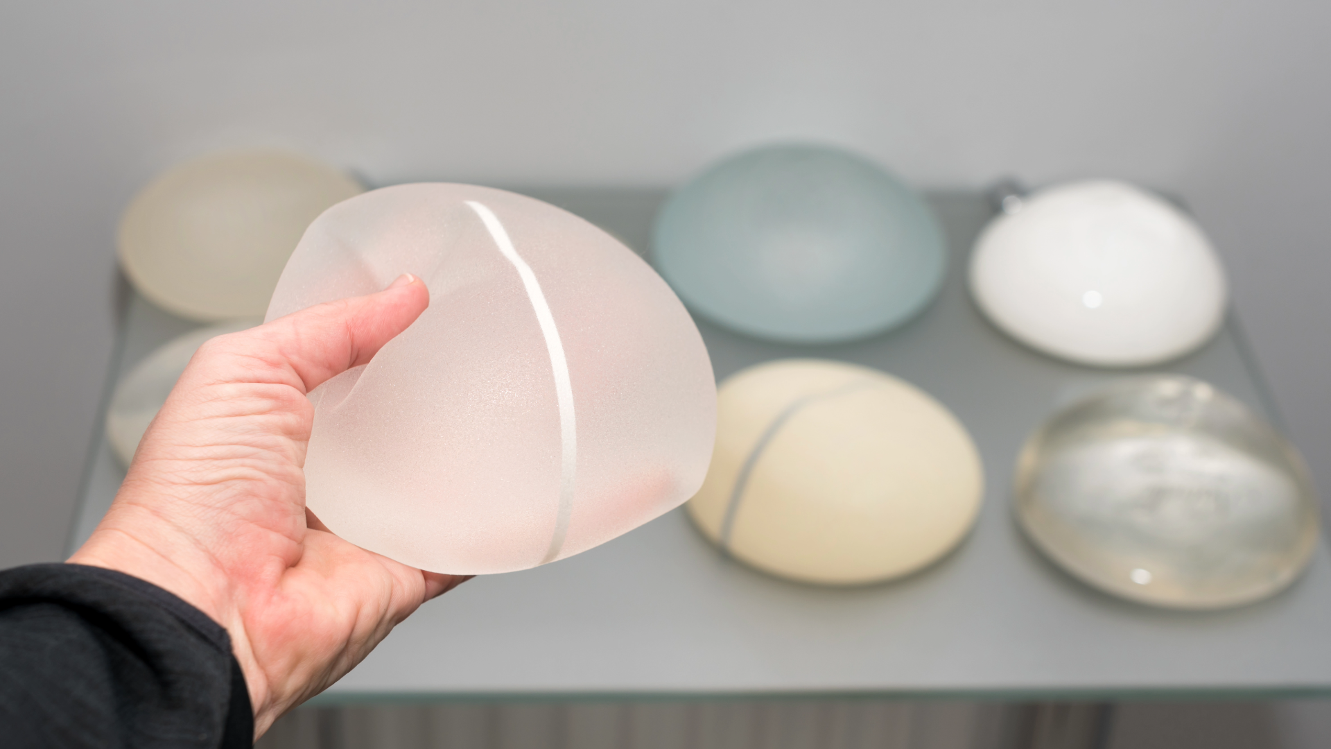 Hand holding a frosted pink glass orb with a white seam, displayed among pastel glass stones on a shelf.
