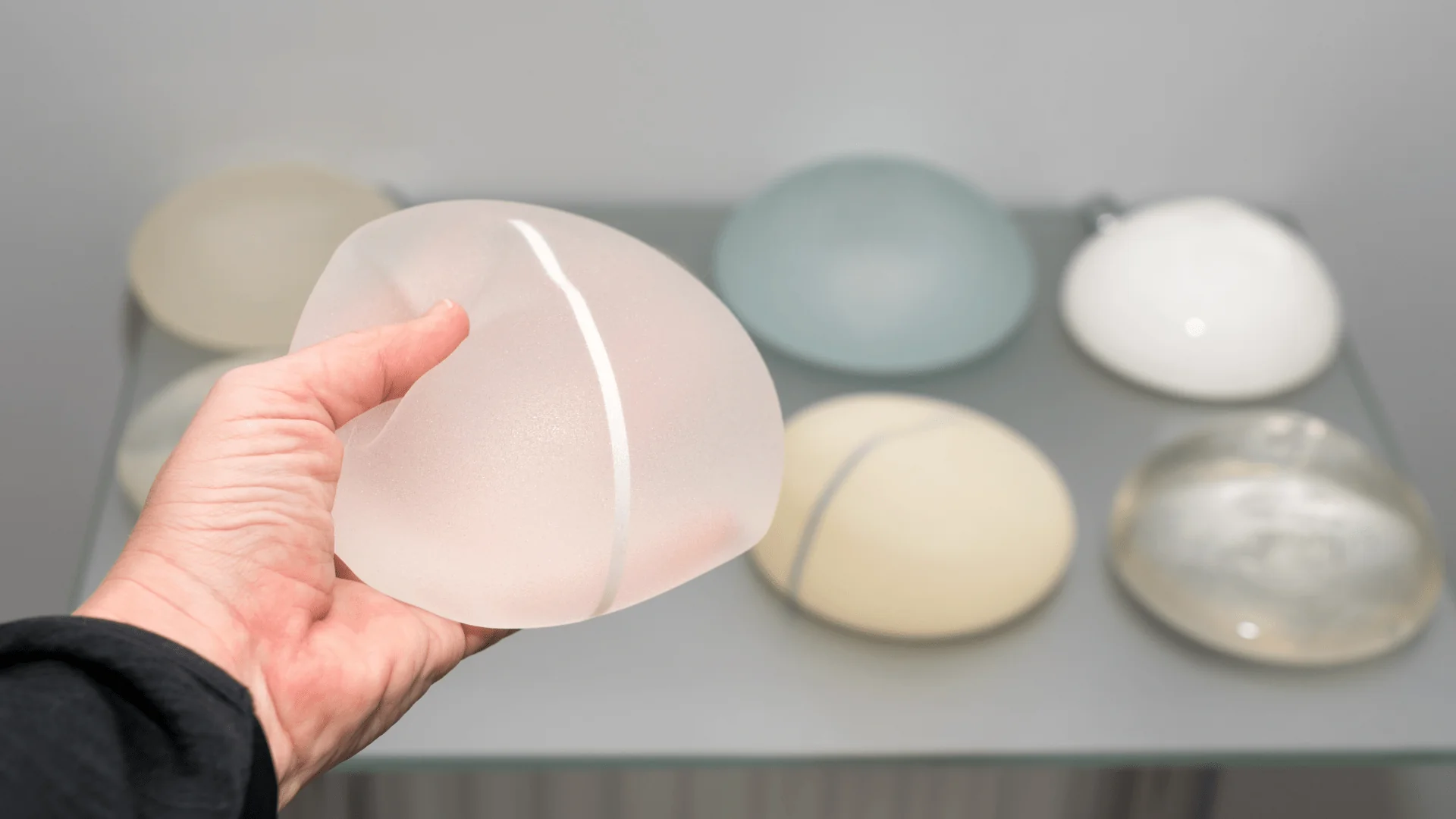 Hand holding a frosted pink glass orb with a white seam, displayed among pastel glass stones on a shelf.