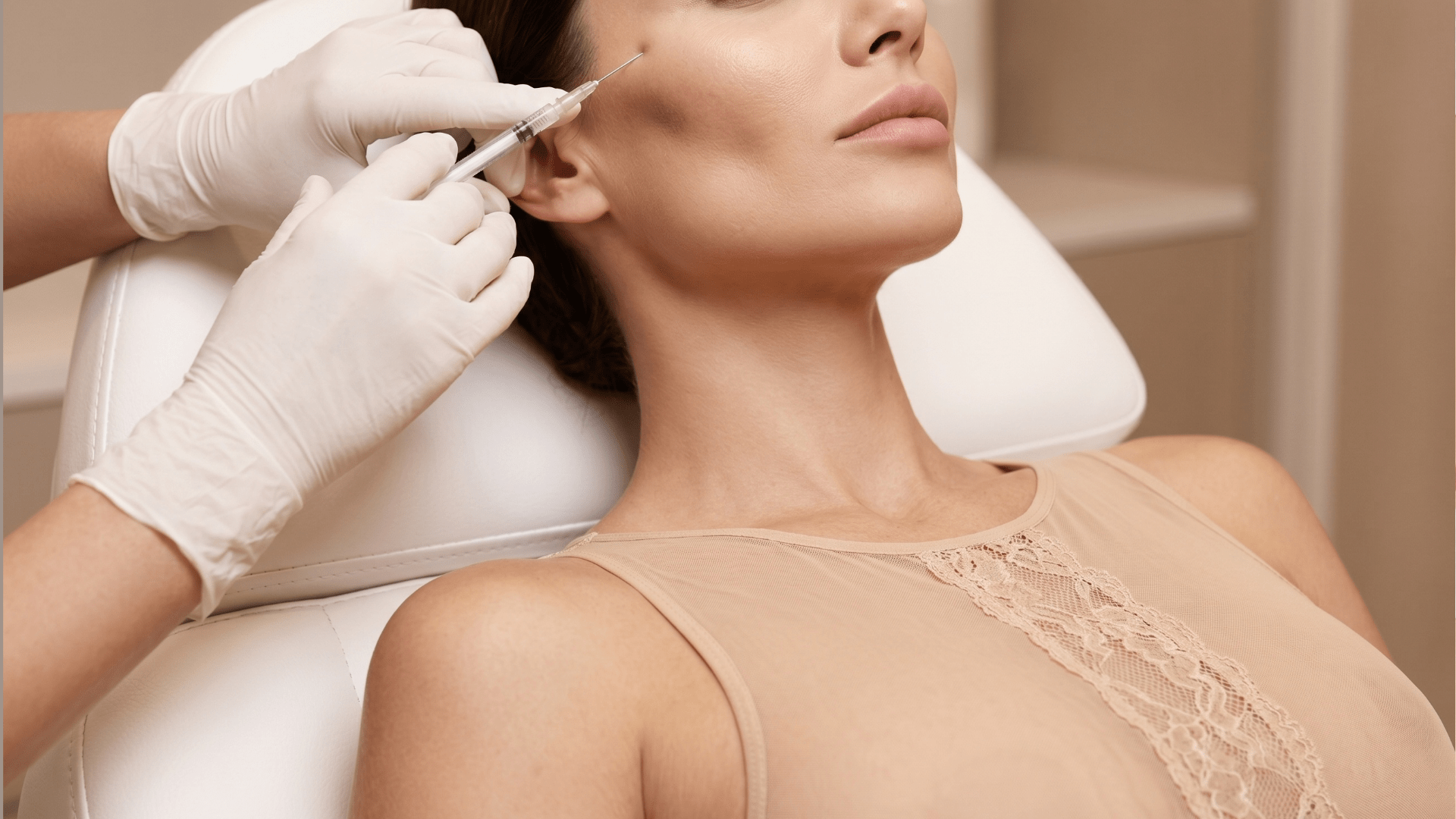 Cosmetic procedure: a clinician administers a facial injection near the jawline of a woman reclining in a treatment chair.