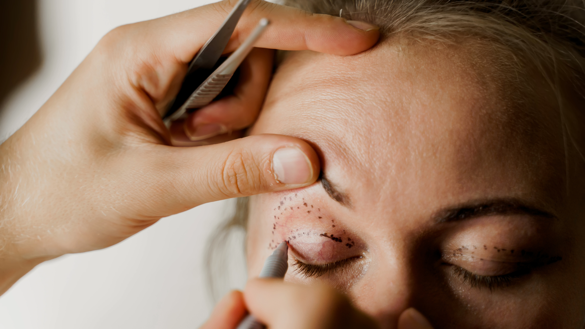Close-up of a cosmetic procedure: a technician uses a tool near a client's eye with dotted markings around the eye for semi-permanent makeup, awaiting eyeliner.