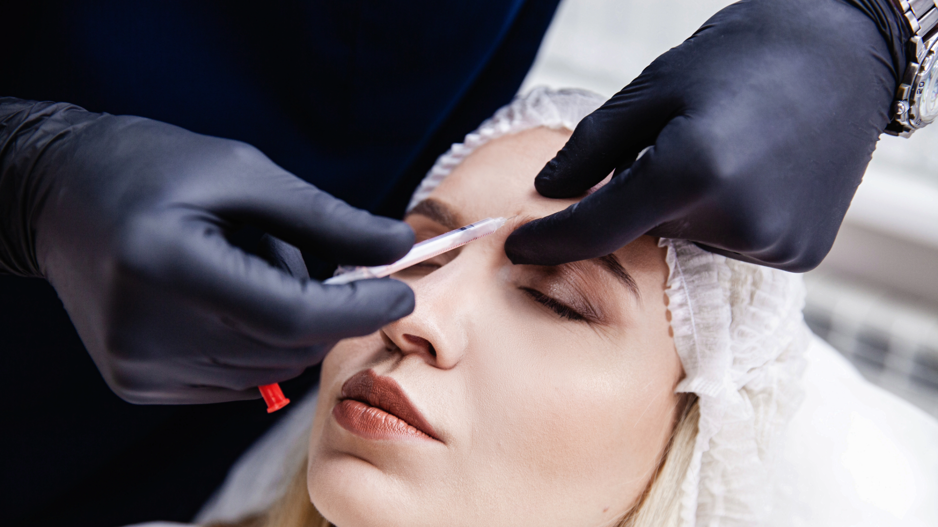 Close-up of a medical professional giving an eye-area injection to a woman with eyes closed.