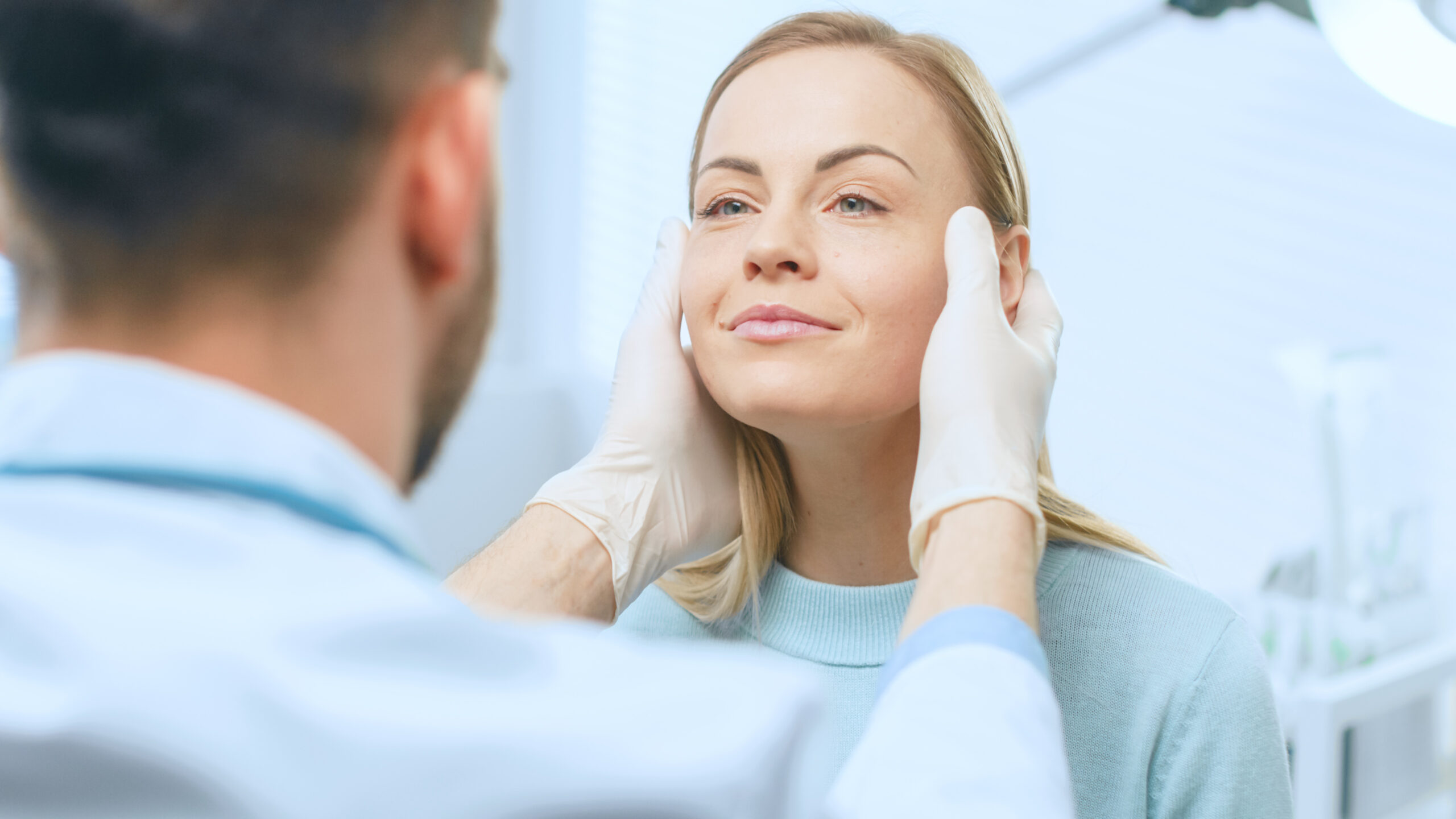 Doctor wearing gloves holding a woman's face for a medical exam in a clinical setting.