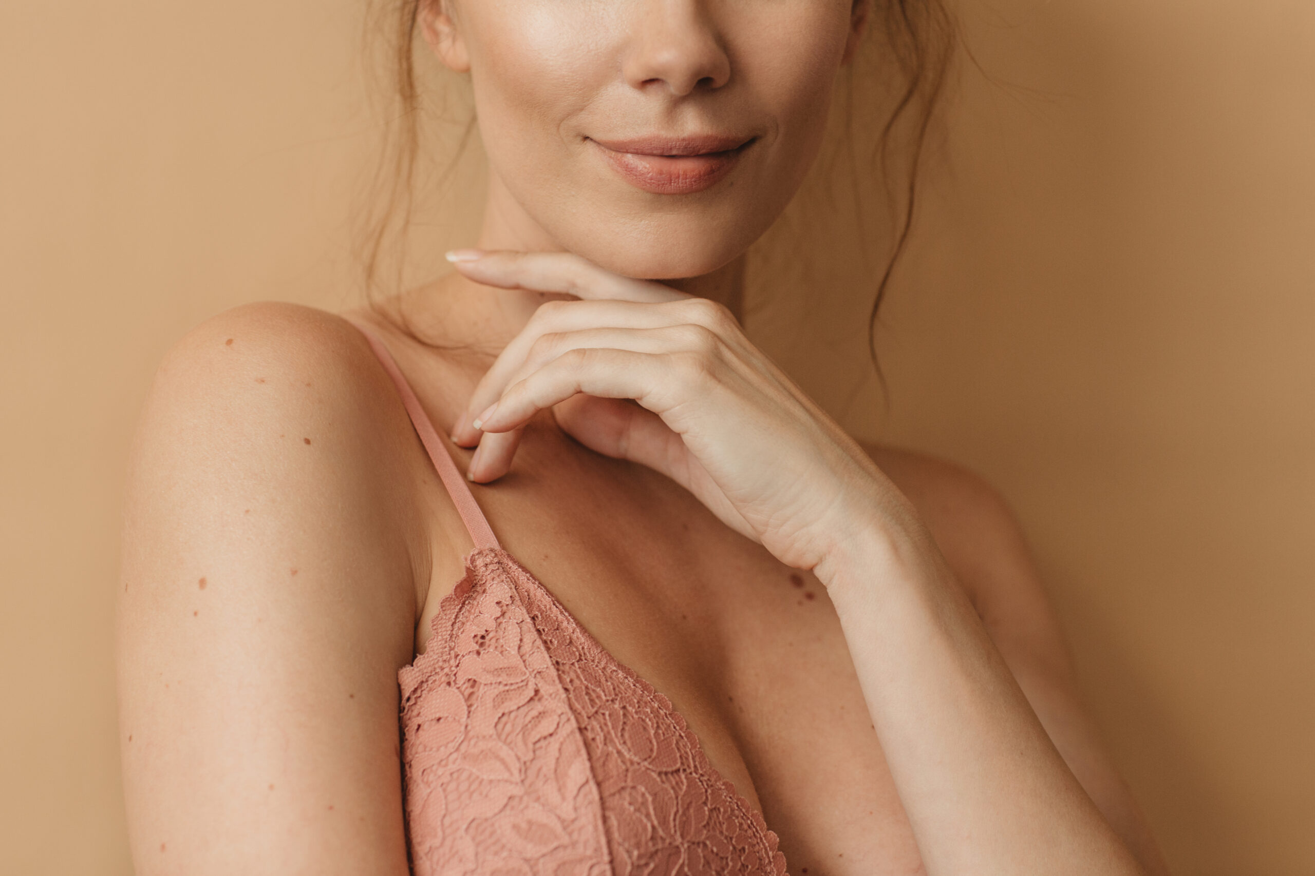 Woman beauty portrait - Dr. Pumberger Partial close-up of a woman's lower face and neck, hands resting under her chin, wearing a pink lace top.