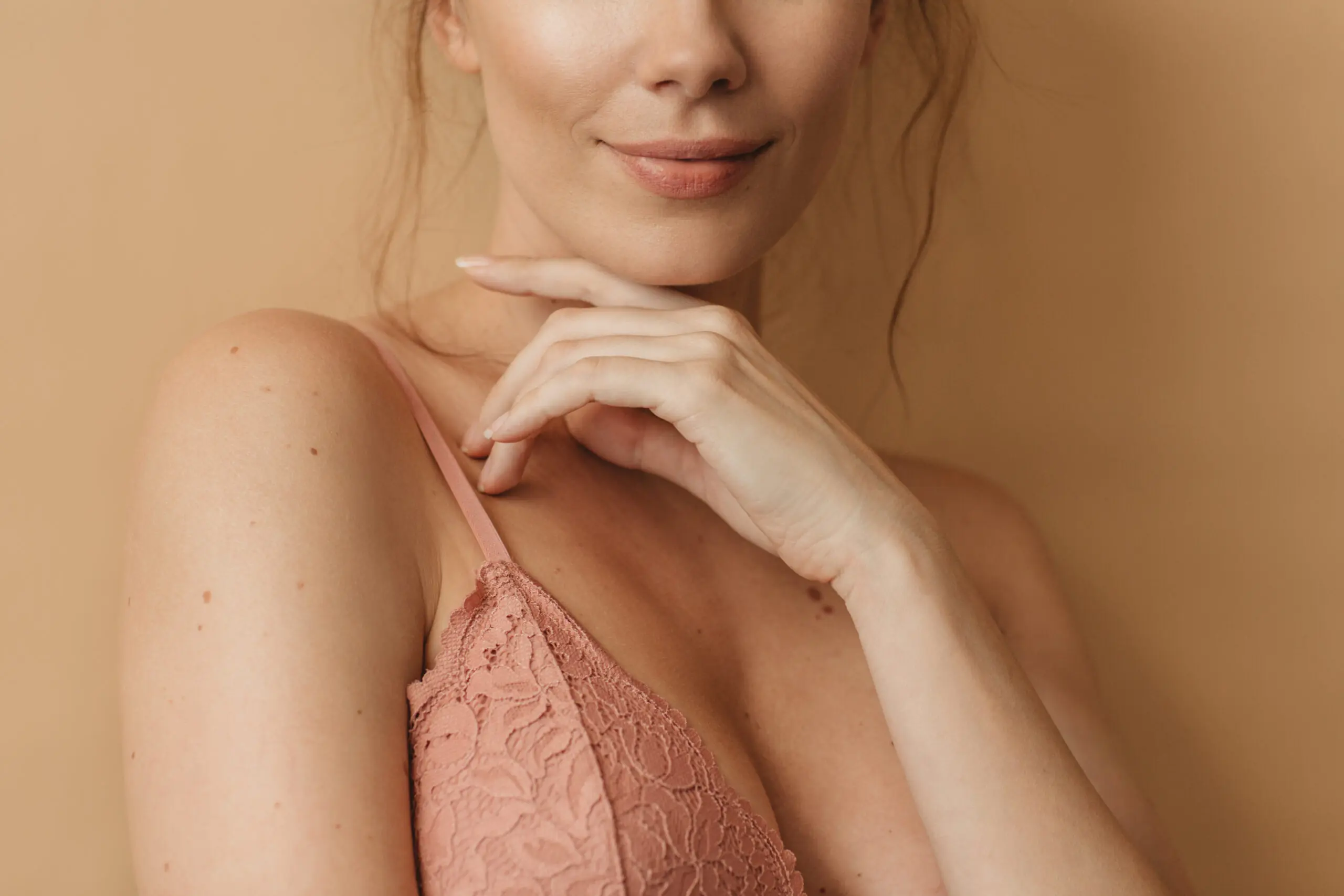 Woman beauty portrait - Dr. Pumberger Partial close-up of a woman's lower face and neck, hands resting under her chin, wearing a pink lace top.